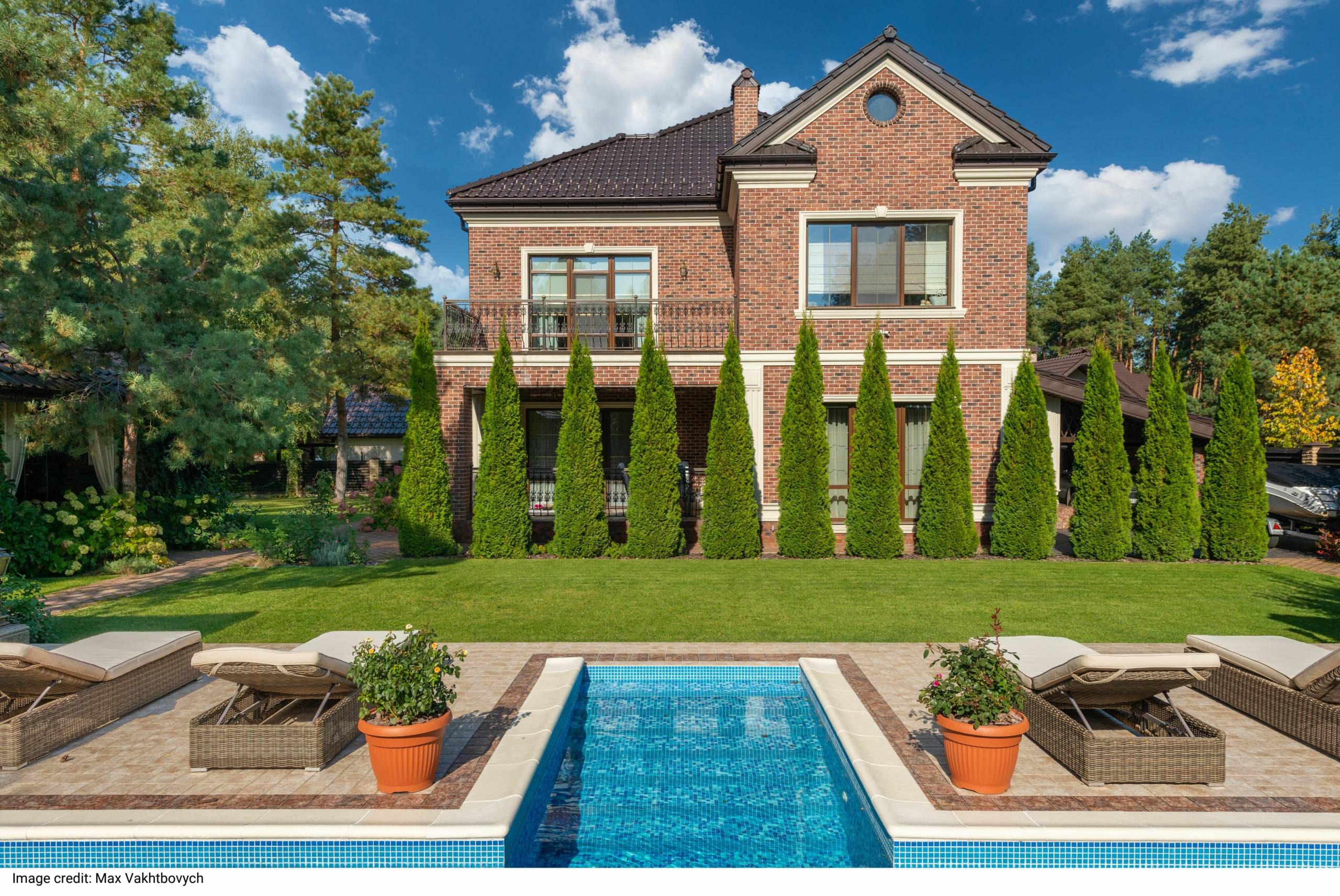 Facade of brick dwell villa with green bushes on lawn and sunbeds near swimming pool by Max Vakhtbovych Facade of brick dwell villa with green bushes on lawn and sunbeds near swimming pool