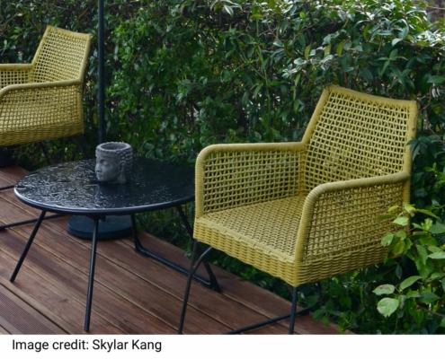 Comfortable wicker rattan armchairs with round table an lamp placed near lush green vegetation in backyard of tropical resort on rainy day