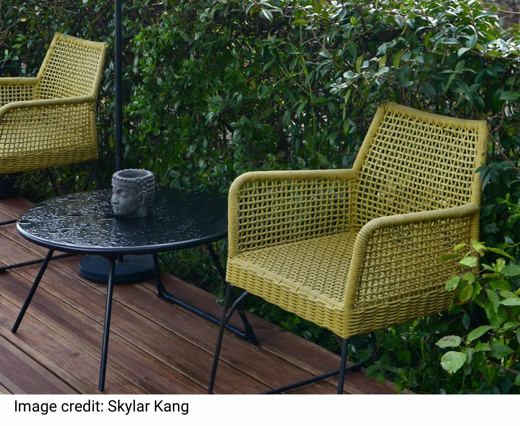 Comfortable wicker rattan armchairs with round table an lamp placed near lush green vegetation in backyard of tropical resort on rainy day