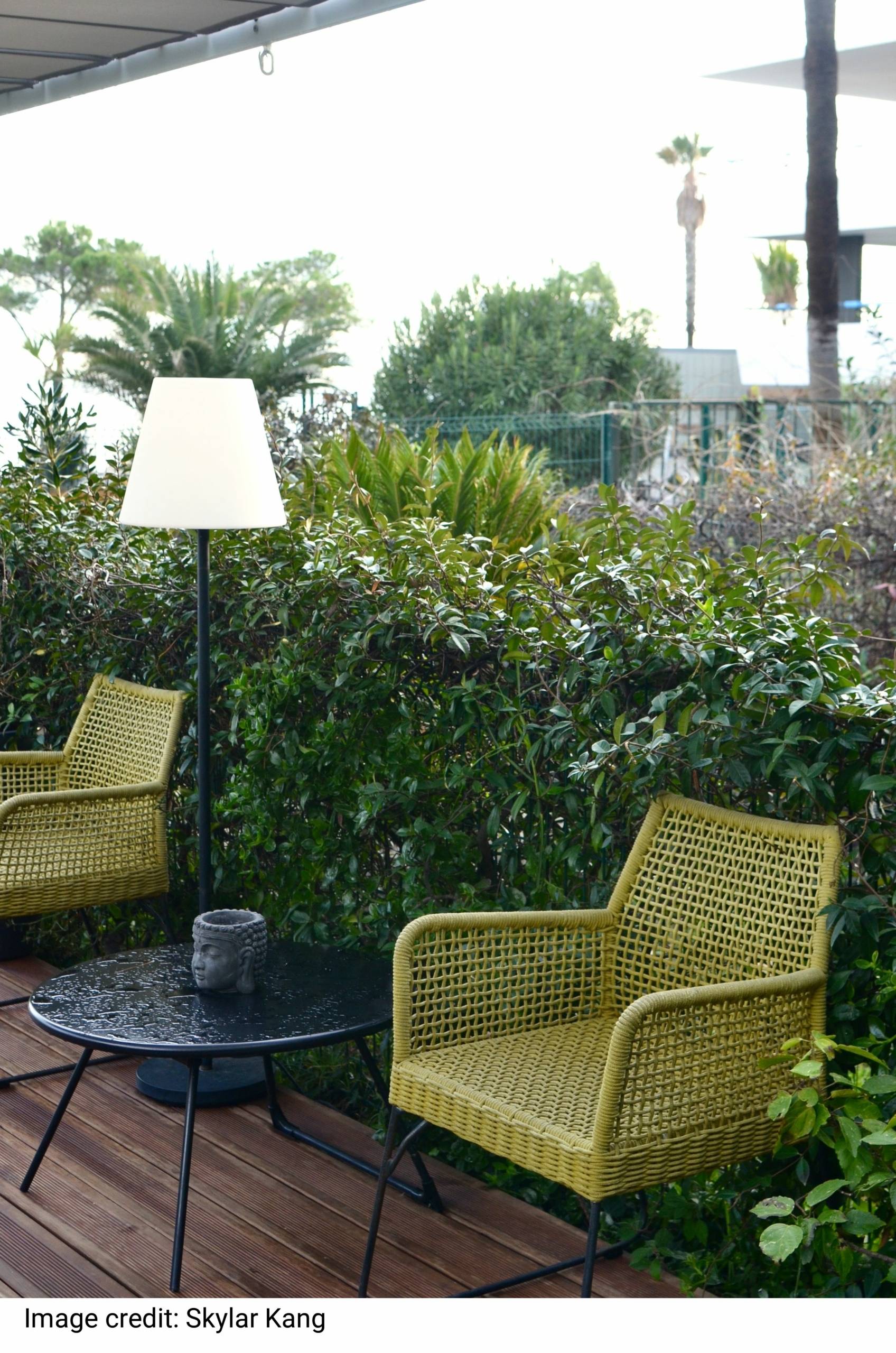 Comfortable wicker rattan armchairs with round table an lamp placed near lush green vegetation in backyard of tropical resort on rainy day