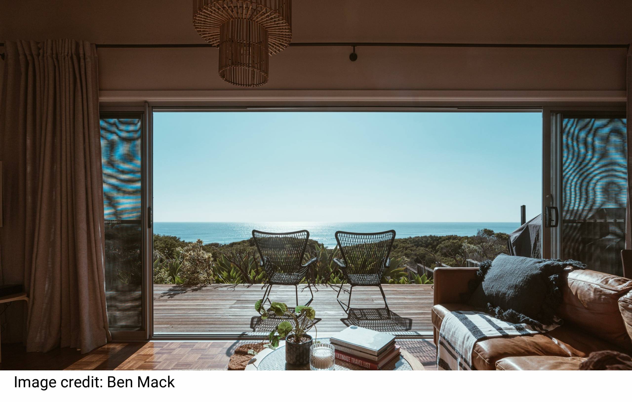 Interior design of luxurious apartment with large balcony doors and wooden terrace having picturesque view on green forested seashore and calm blue sea